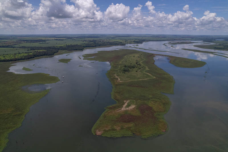 imagem 1, local: Iturama-MG. Imagem aérea, a câmera aponta para o horizonte. Vemos o rio Grande em sua extensão, no meio do rio há uma ilha, uma grande extensão de terra coberta de vegetação com algumas árvores no centro. O céu é azul com nuvens de variados formatos espalhadas por todo o quadro até a linha do horizonte. Áreas cobertas por mata aparecem na margem esquerda do rio e mais ao fundo, o restante são áreas de agricultura.